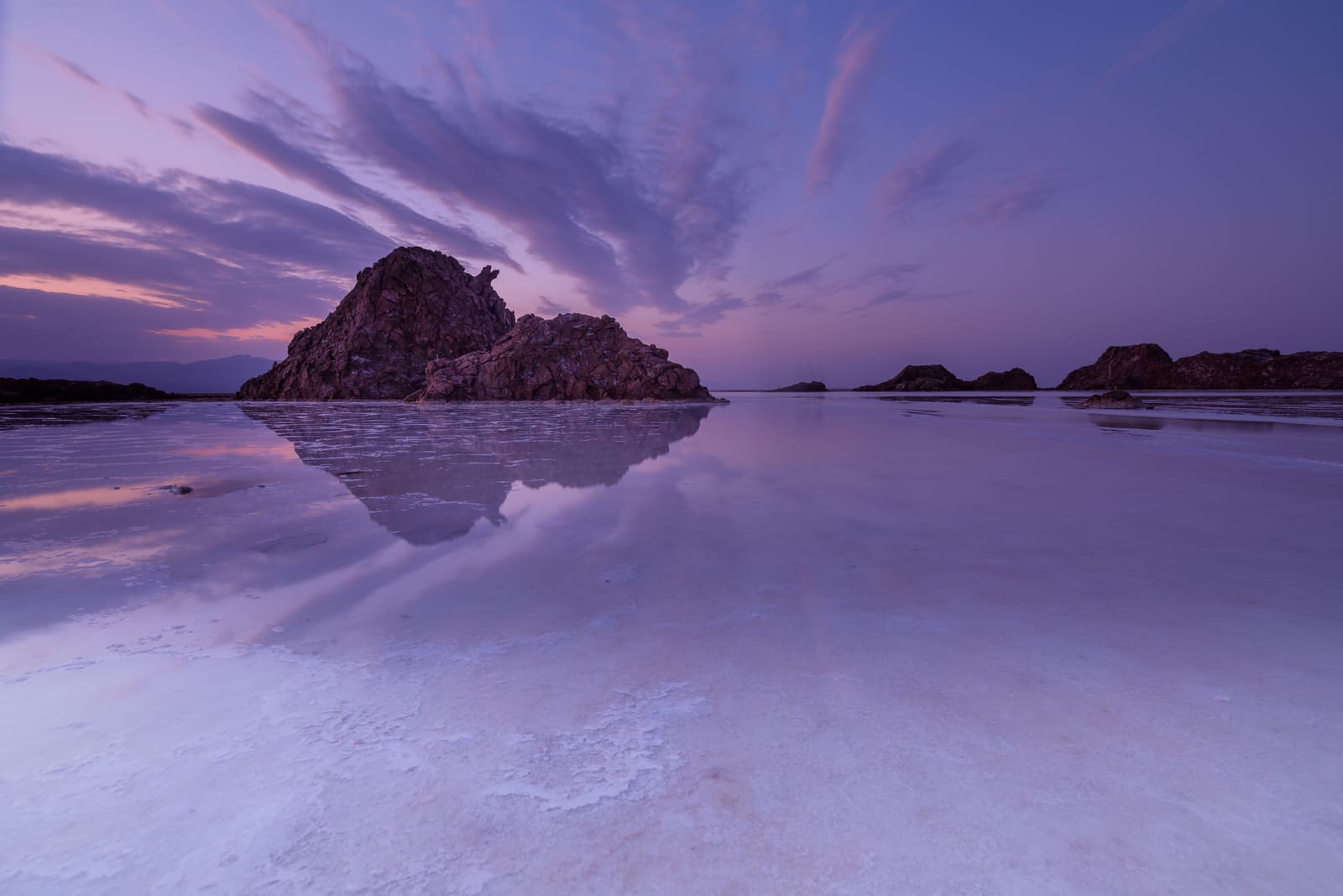 Le saline del lago Assale tinte di viola al tramonto con colline lontane
